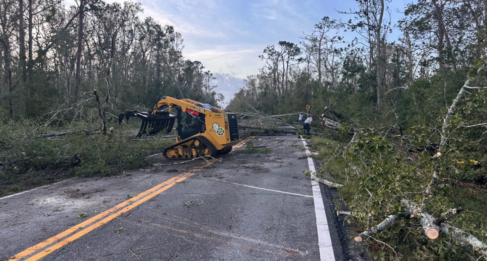 The aftermath of Hurricane Helene, showing the destruction caused by the storm, including damaged buildings, fallen trees, and debris scattered across roads, with recovery efforts in progress.